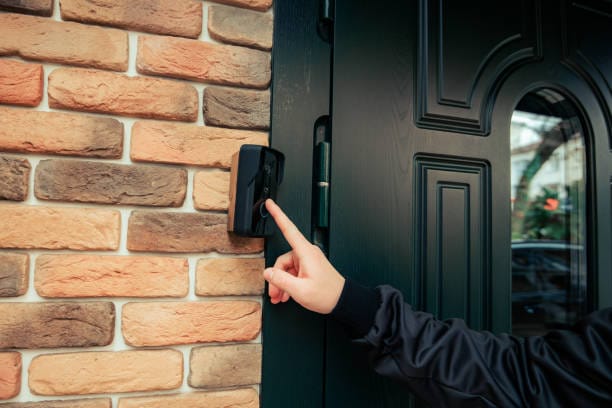 man hand in a black jacket rings the door intercom orange brick wall