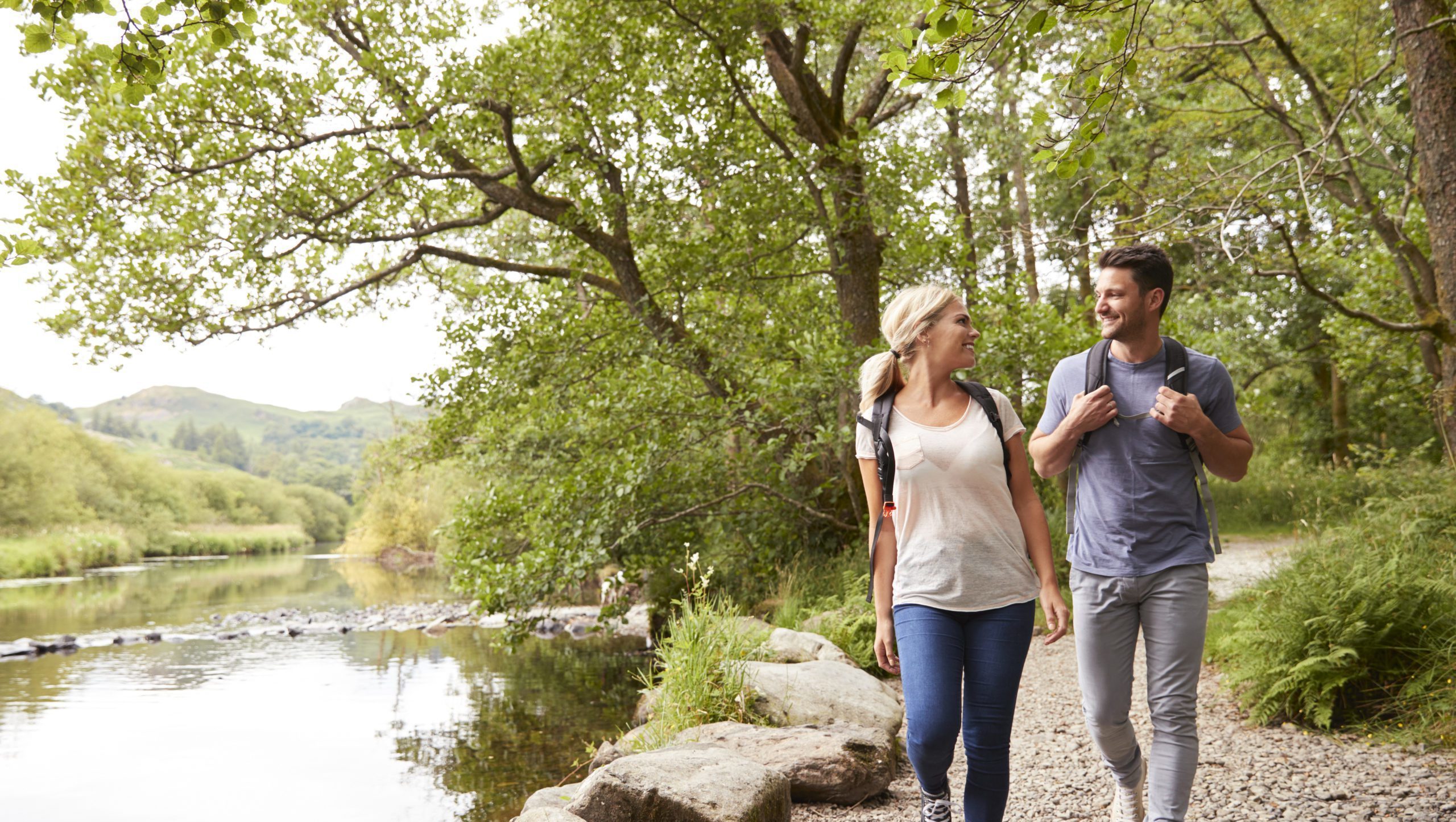 Couple Hiking Along Path By River In UK Lake District