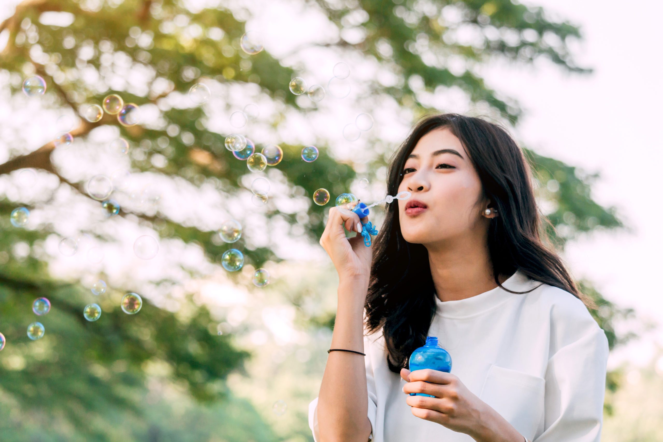 Beautiful Woman Blowing Bubbles While Standing Against Sky In Park