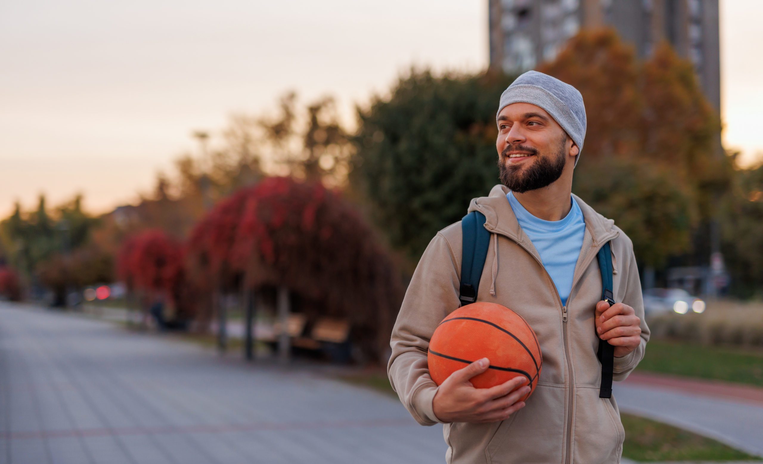 Smiling man with basketball at sunset in urban environment