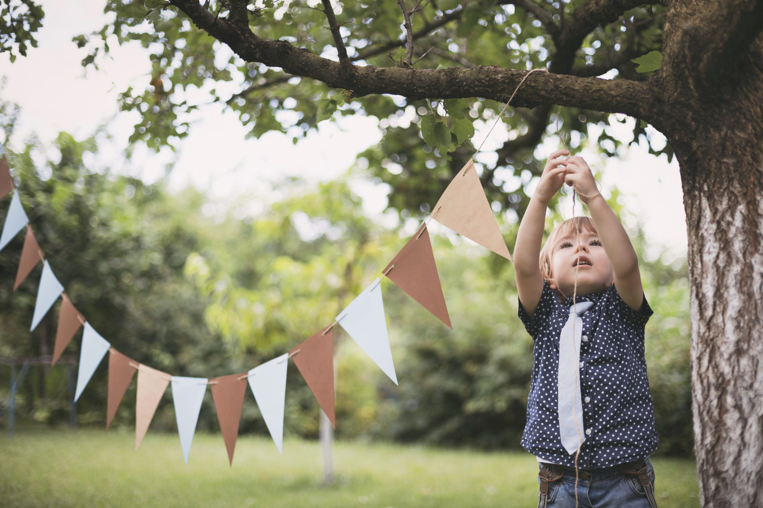 Cute little child getting ready for a garden party or outdoor birthday party by decorating with pennant