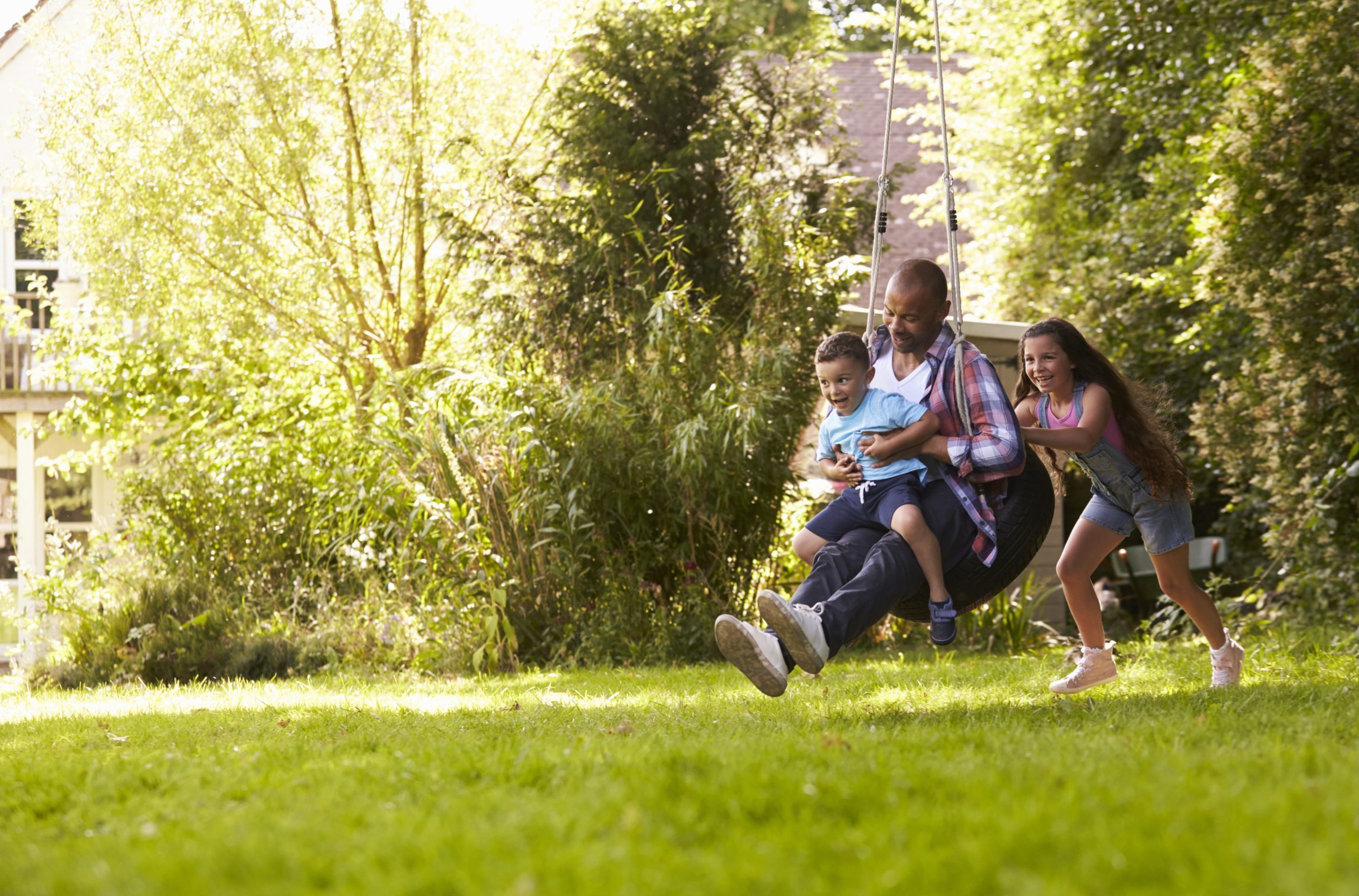 Daughter Pushing Father And Son On Tire Swing In Garden