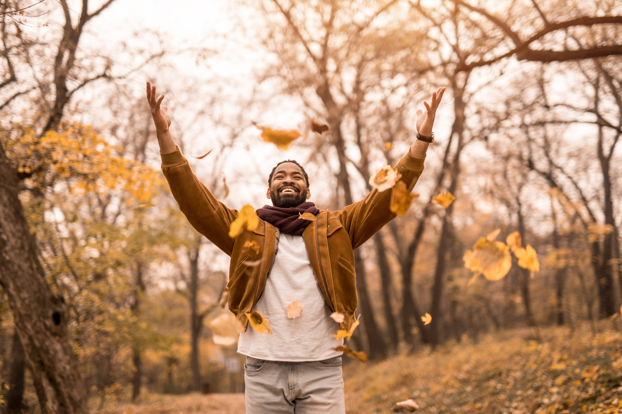 Happy young African American man throwing leaves in beautiful autumn park