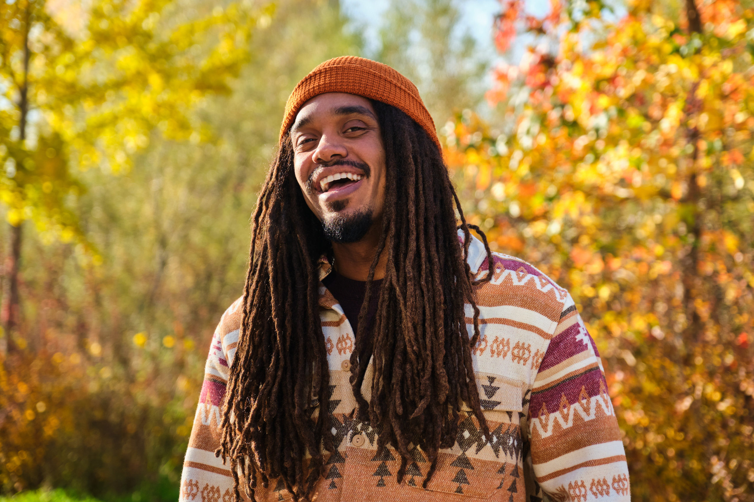 African young man with dreadlocks laughing and looking at camera in fall