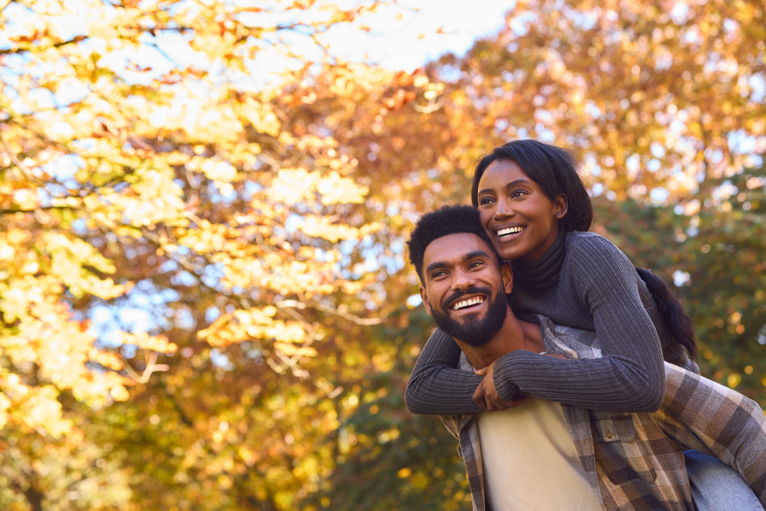 Loving Young Couple With Man Giving Woman Piggyback Against Background Of Autumn Leaves