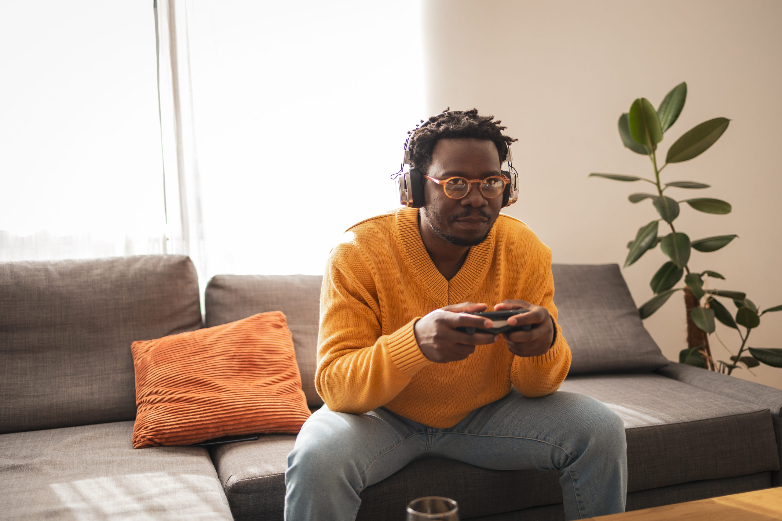 Young man enjoying video gaming with headphones on in cozy living room